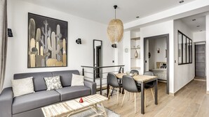 Ein modernes Wohnzimmer mit einem grauen Sofa, einem Esstisch mit Stühlen und einer großen Wandkunst mit einem Kaktus.