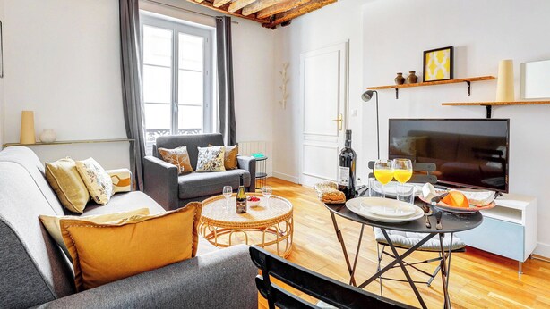 Uma sala de estar moderna com um sofá, uma mesa de jantar com cadeiras, uma televisão e uma janela com cortinas.