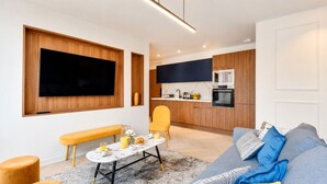Una sala de estar moderna con un sofá, una mesa de centro y un banco. Hay una zona de cocina con un microondas y un lavamanos.