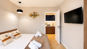 Habitación de hotel con cama, televisor de pantalla plana, una obra de arte en la pared y una kitchenette al fondo.