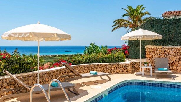 Un espace aménagé au bord de la piscine, avec des chaises longues, des parasols et une vue sur la mer.