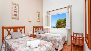 Une chambre avec deux lits, une fenêtre donnant sur la mer et une chaise en bois.