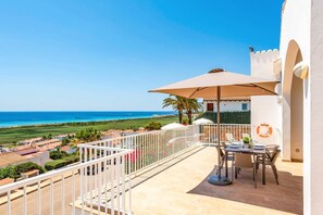 A balcony with a table and chairs, overlooking a beach and ocean.