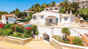 Une villa blanche avec une piscine, entourée d’une végétation luxuriante et sous un ciel d’un bleu limpide.