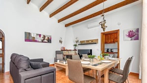 Un coin repas avec une table en bois, des chaises et un téléviseur. On aperçoit un canapé et une cheminée au fond.