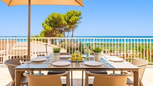 Une table à manger dressée avec des assiettes, des verres et une bouteille, donnant sur une plage sous un ciel dégagé.