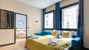 A hotel room with a bed, a window with blue curtains, a view of buildings outside, and a door leading to another room. - TBS 60 - Spacious and elegant apartment (Paris)
