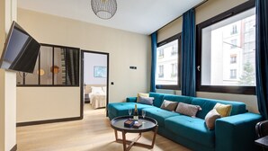 A modern living room with a teal sofa, a coffee table, and a TV mounted on the wall. - TBS 60 - Spacious and elegant apartment (Paris)