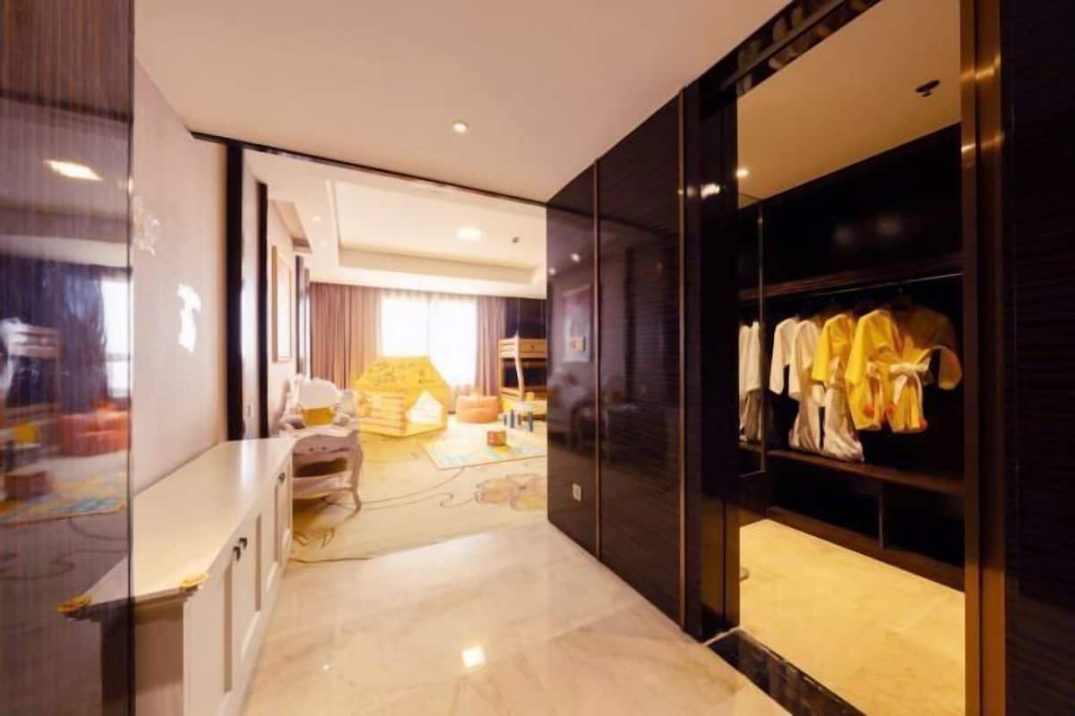 Une chambre d’hôtel moderne avec un sol en marbre, une grande armoire où sont suspendus des vêtements et un espace lit bien visible.