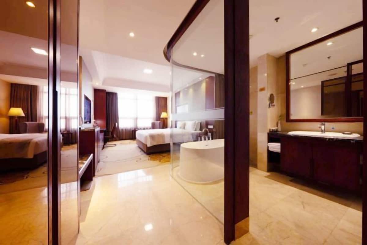 Une chambre d’hôtel comprenant un lit, un coin salon, un grand miroir et une baignoire.