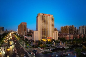 Un hotel de gran altura con varios pisos, una entrada destacada y una calle concurrida al fondo.