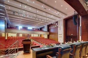 Een congreszaal met een tribune, een lange tafel met stoelen en een podium.