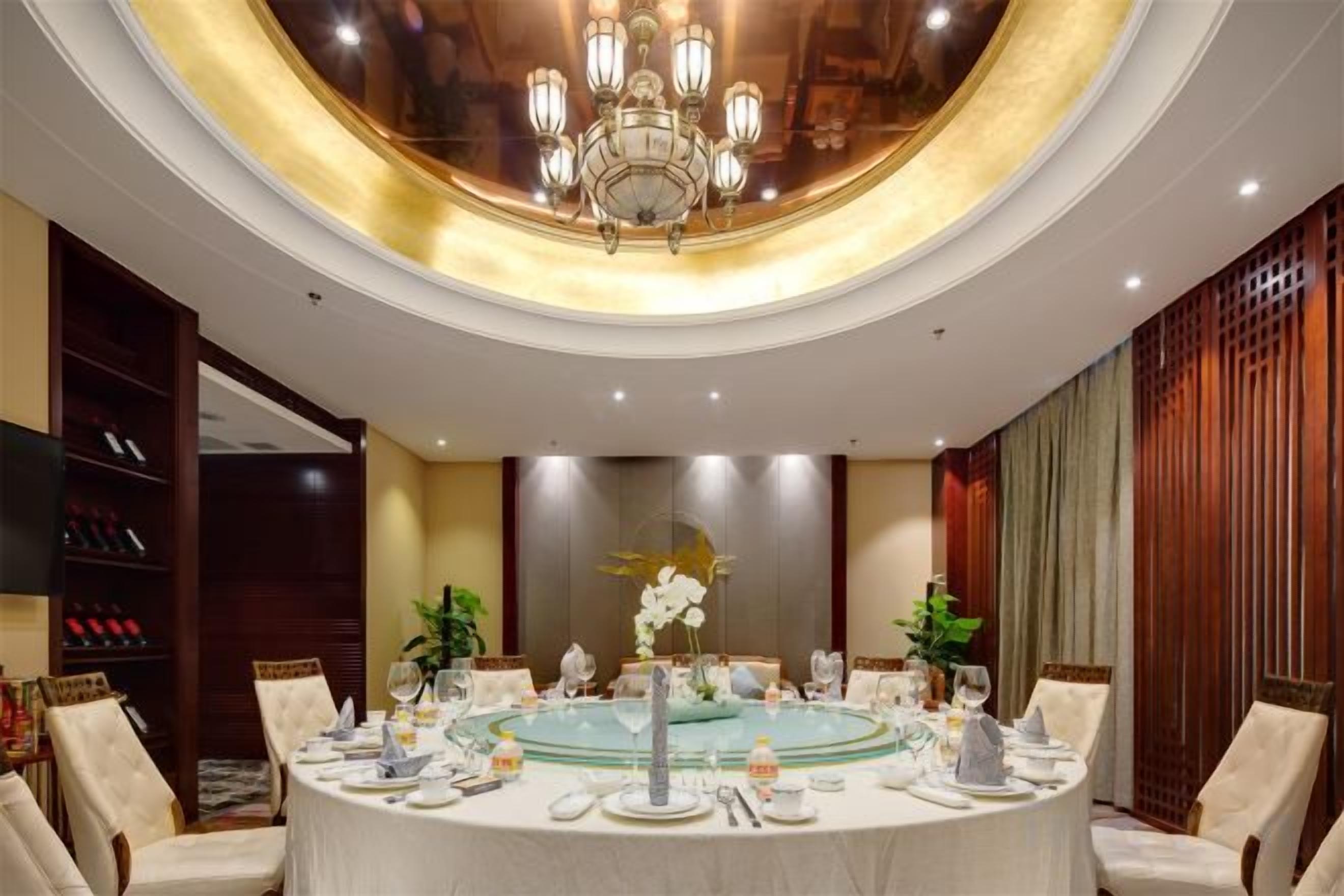 A round table set for a formal event, surrounded by chairs, with a chandelier above.