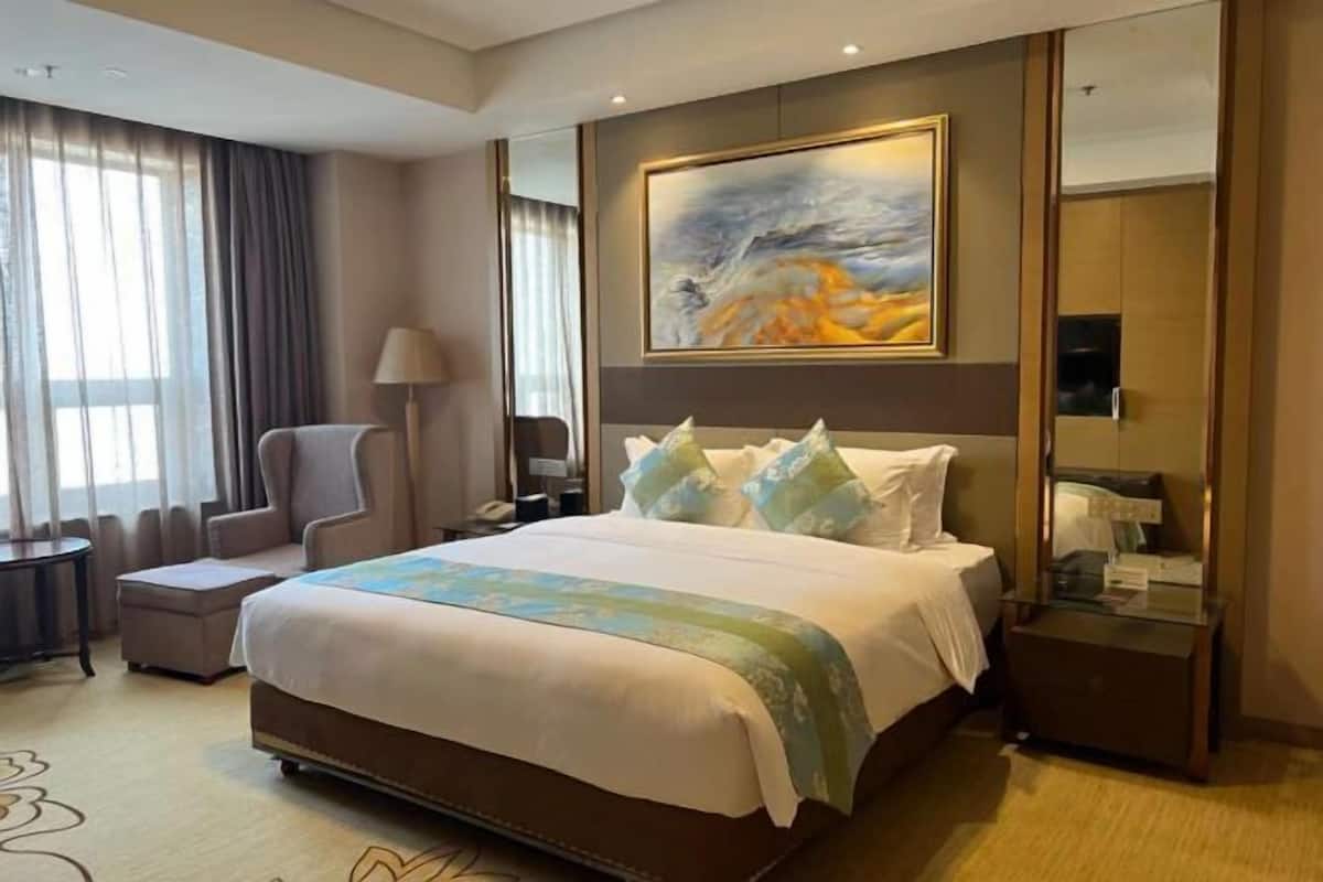 Une chambre d’hôtel avec un grand lit, une chaise, une table de chevet, une lampe et un tableau au mur.
