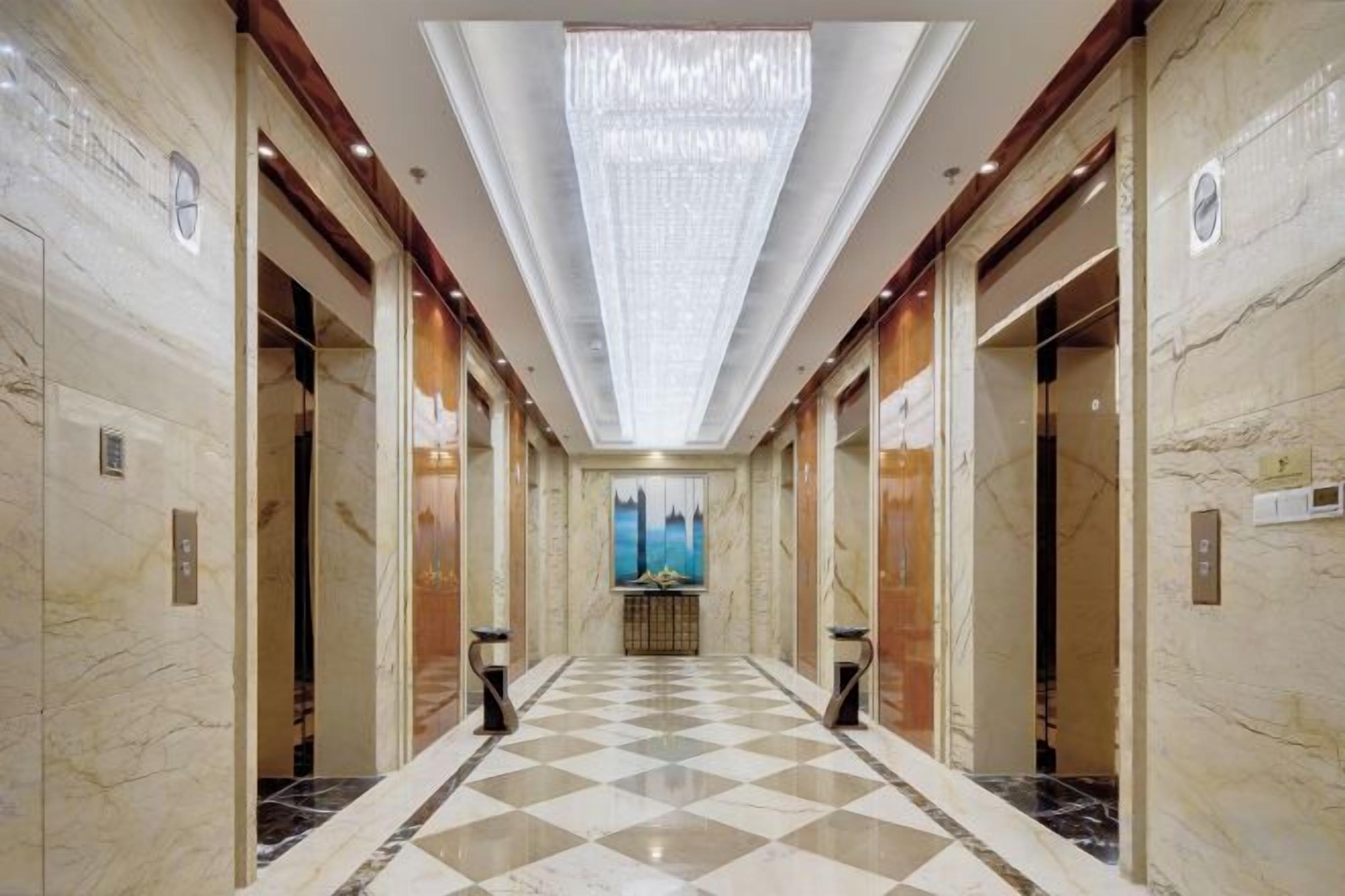 A hotel hallway with marble floors, a chandelier, and doors leading to rooms.