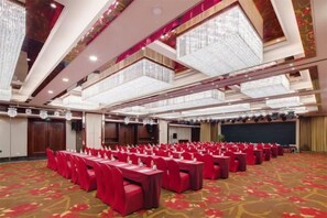Un salón de banquetes con filas de mesas y sillas, un techo alto con candelabros y un piso alfombrado.