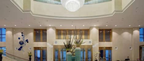 A spacious lobby with a grand chandelier, a central fountain, and a staircase leading to upper levels.