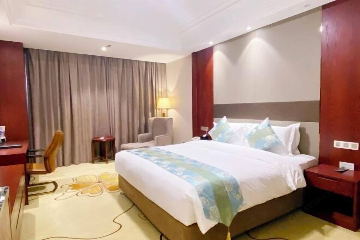 Une chambre d’hôtel avec un grand lit, un bureau, une chaise, une lampe et un rideau.