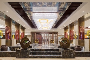Un hall d’hôtel avec un comptoir de réception en marbre, un grand lustre et un décor traditionnel.