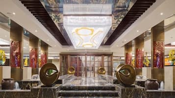 A hotel lobby with a grand staircase, a large chandelier, and decorative columns.