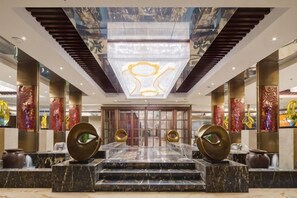 En hotellobby med en storslagen trappa, en stor kristallkrona och dekorativa pelare.