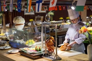 Un chef préparant des plats dans une cuisine décorée de différents drapeaux, avec une vitrine contenant des produits alimentaires.