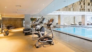 Een modern binnenzwembad met fitnessapparatuur, een glazen wand en uitzicht op de bovenverdieping.