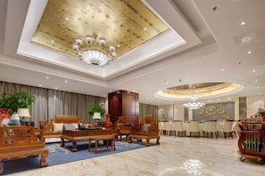 Un hall amplio con techo alto, candelabros y una zona de estar con mobiliario de madera.