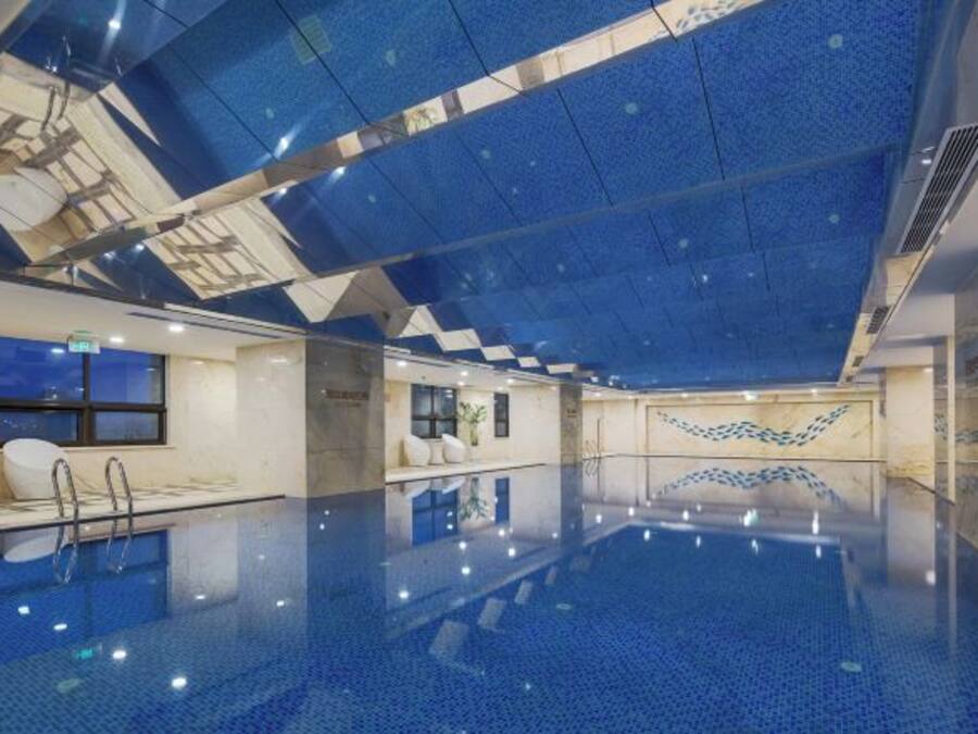An indoor swimming pool with a geometric ceiling design, clear glass walls, and a clean, modern aesthetic.
