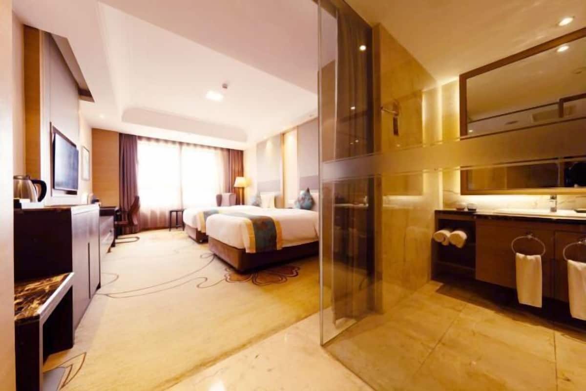 Une chambre d’hôtel comprenant un lit, un bureau, une chaise, une télévision, une salle de bain avec un miroir et une douche.