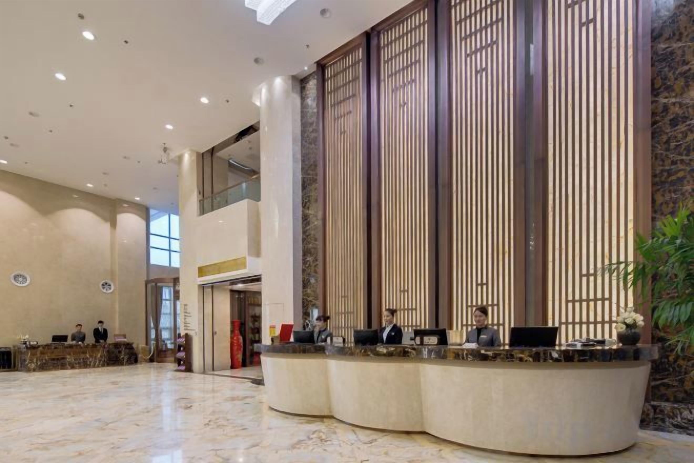 A hotel lobby with a reception desk, seating area, and a large vertical wooden panel.