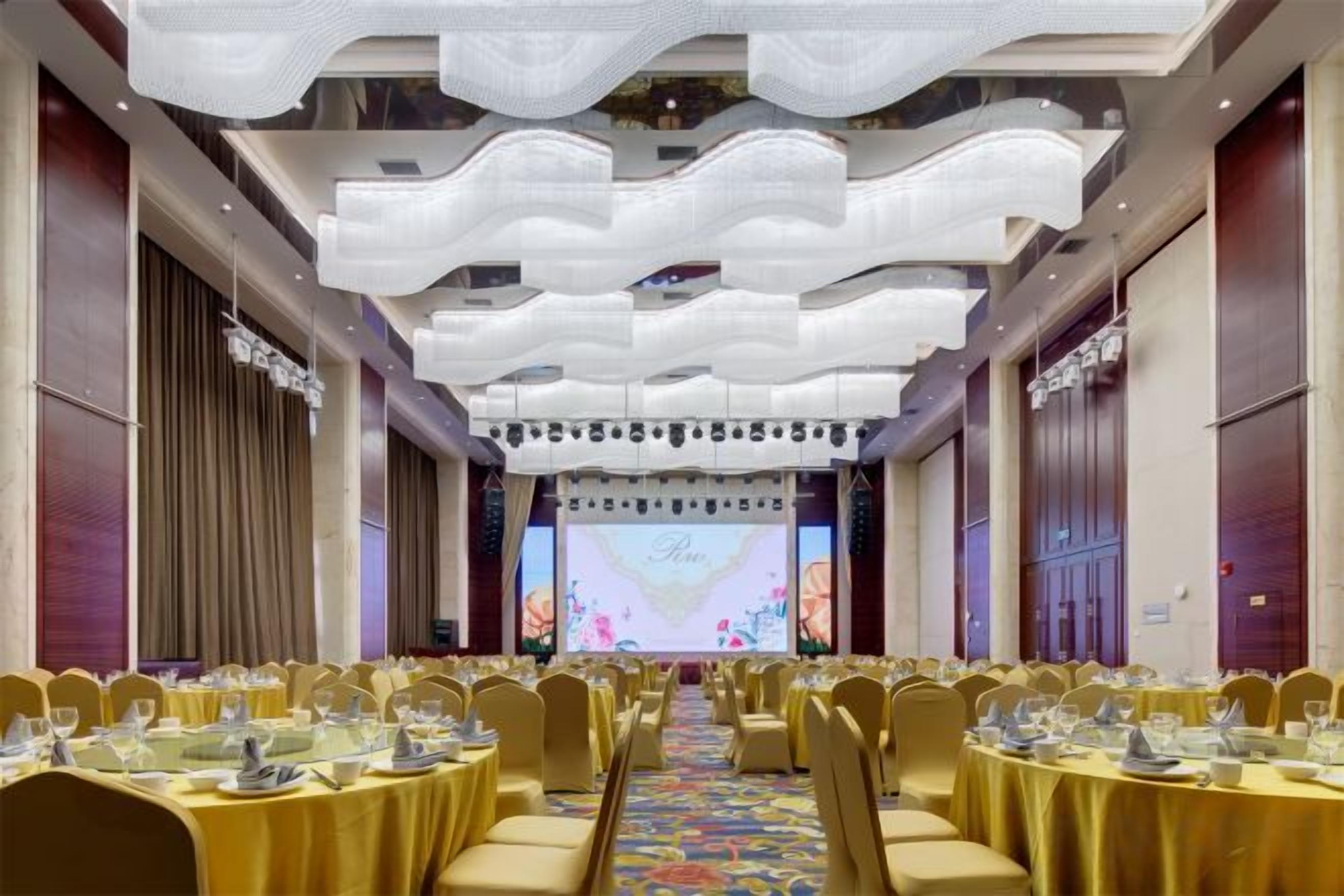 A banquet hall with round tables, chairs, and a stage with a large screen.