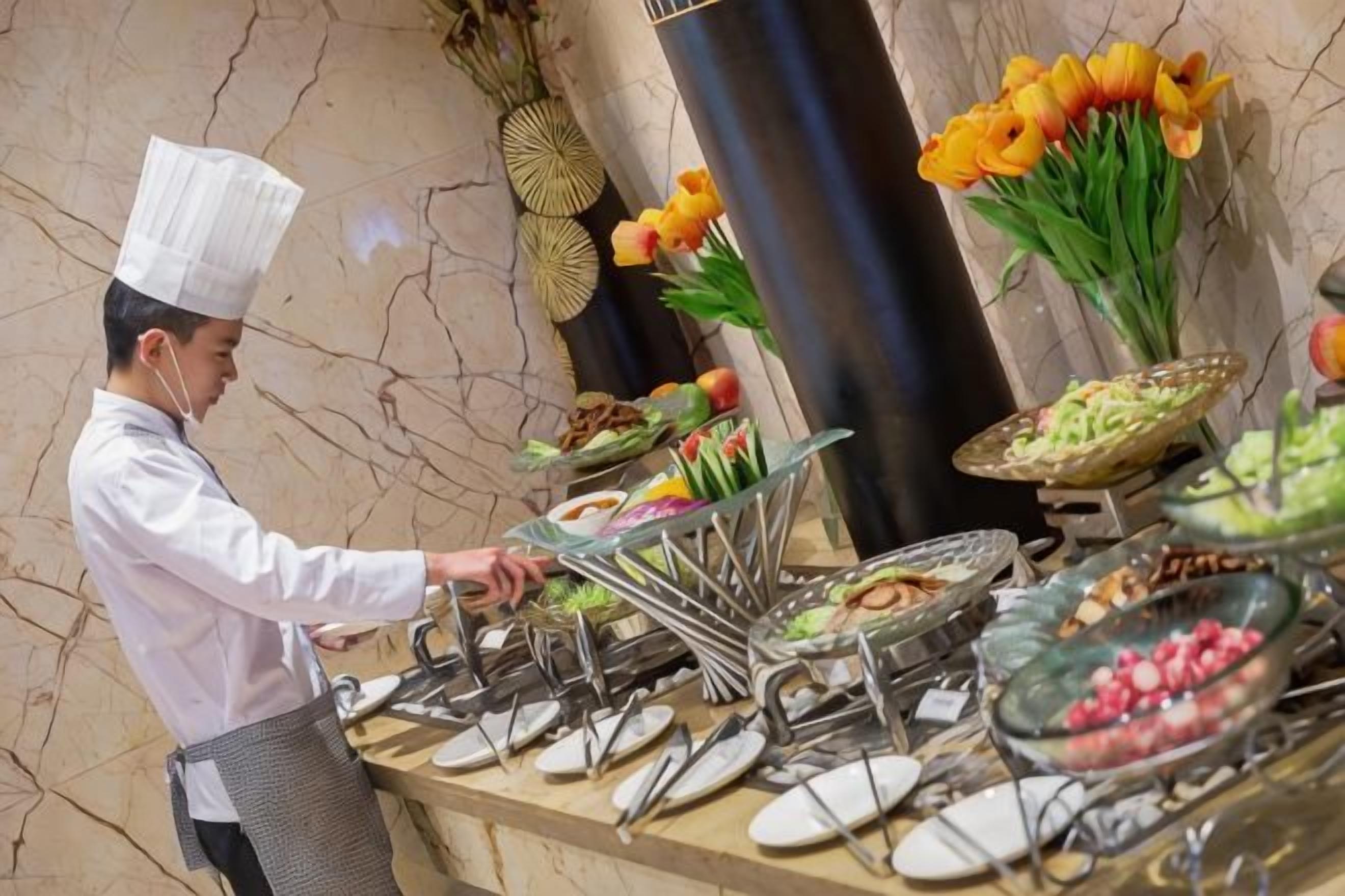 A buffet setup with various food items and a waiter serving.