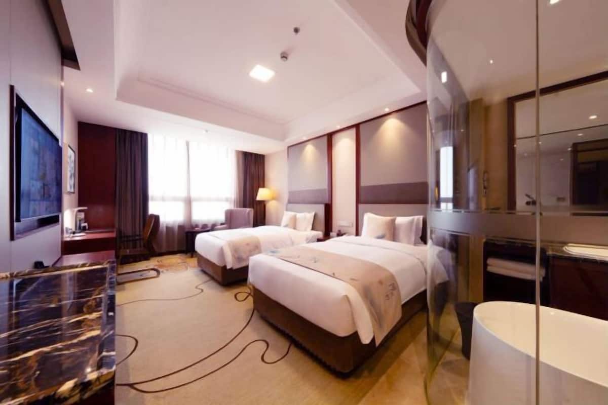 Une chambre d’hôtel avec deux lits, un bureau en marbre, un grand miroir et une baignoire.