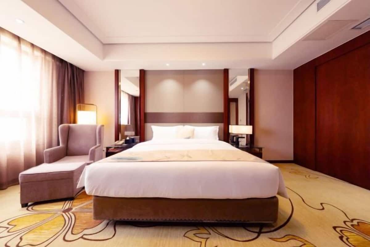 Une chambre d’hôtel avec un grand lit, une chaise, une table de chevet et une lampe.