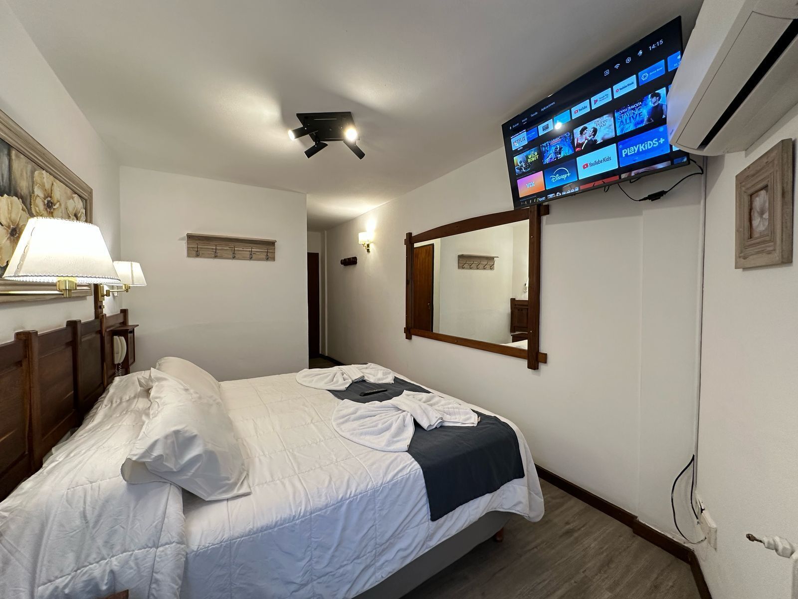 Une chambre d’hôtel avec un lit, un téléviseur fixé au mur diffusant différentes chaînes, une lampe de chevet et un miroir.