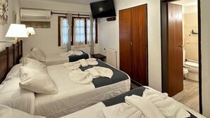 Habitación de hotel con dos camas, televisión, aire acondicionado y baño visible a través de una puerta abierta.