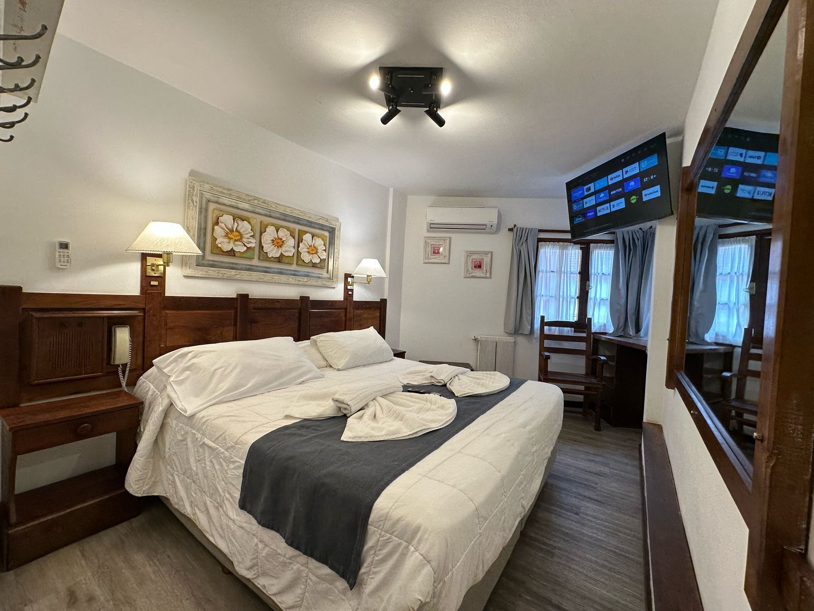 Hotelkamer met een bed, bedlampen, een schilderij, een airconditioning, een televisie en een bureau met stoel.
