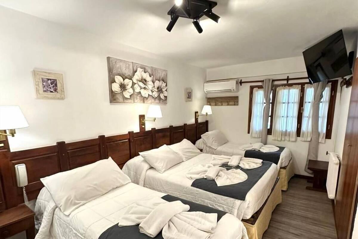 A hotel room with two beds, a TV, an air conditioning unit, and a painting on the wall.