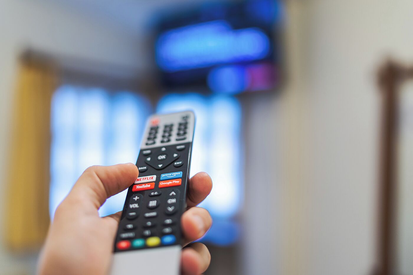 Een hand houdt een afstandsbediening met knoppen voor Netflix, YouTube en Google Play.