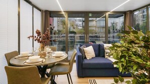 Un salon moderne avec un canapé, une table à manger pour quatre personnes et de grandes fenêtres donnant sur la ville.