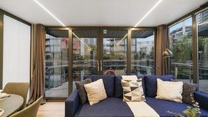 Une chambre d’hôtel moderne, dotée d’un canapé, d’une table à manger et offrant une vue sur la ville grâce à de grandes fenêtres.