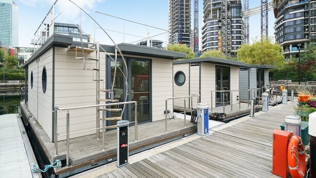 Une structure flottante moderne dotée d’une terrasse, de garde-corps et d’un petit bâtiment avec une porte et des fenêtres.