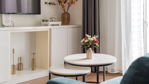 A modern living room with a white console table, a round table with a vase of flowers, and a flat-screen TV mounted above the table.