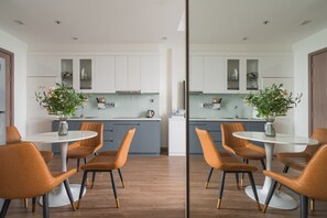 A modern kitchen with white cabinets, a central island with chairs, and two potted plants. - Vinhomes Green Bay Luxury Apartment  (Hanoi)