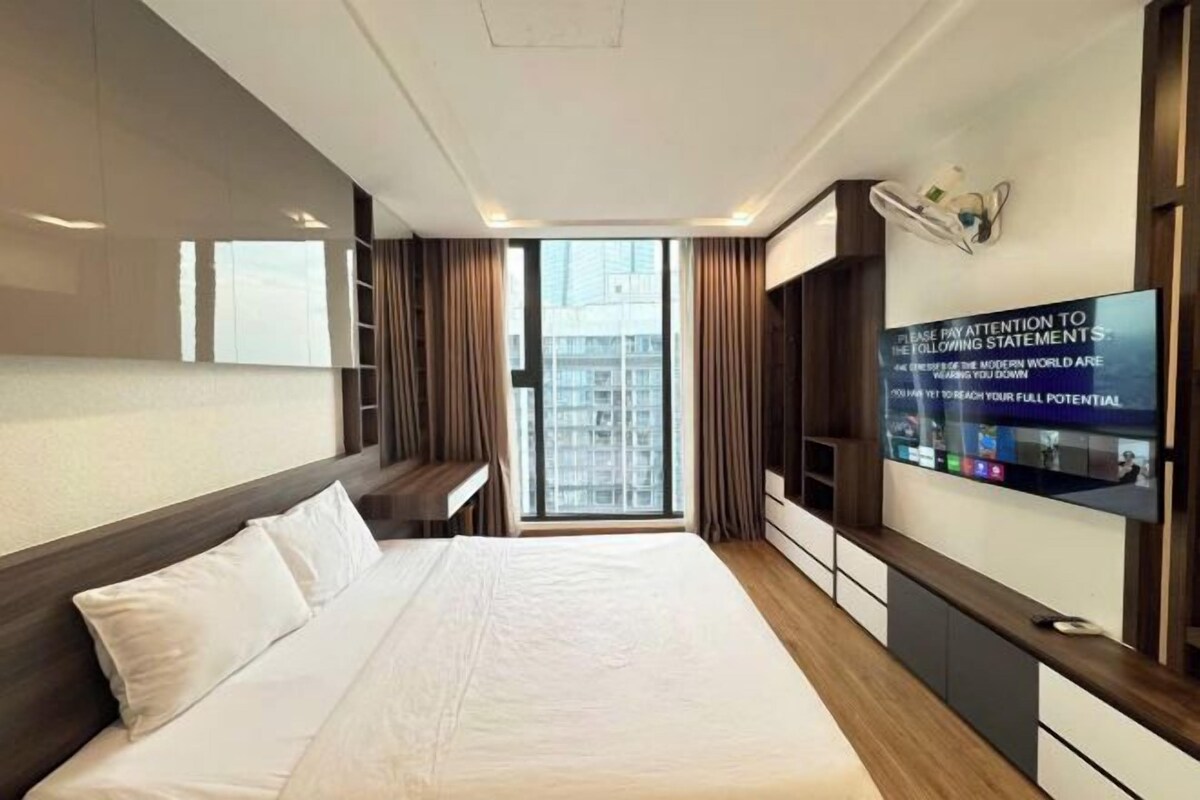 Habitación de hotel con una cama grande, un televisor montado en la pared y vista a la ciudad por la ventana.