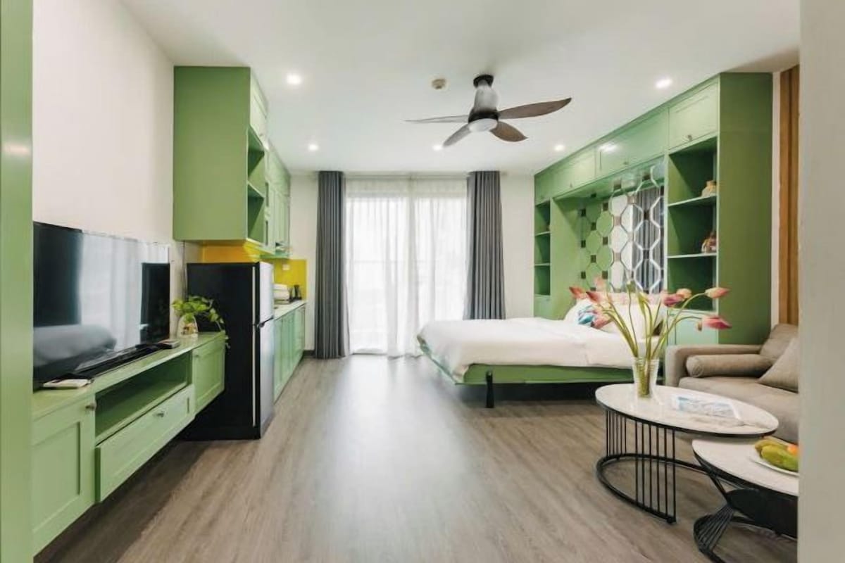 Una habitación de hotel moderna con una cama, un televisor, una mesa de comedor y un ventilador de techo.