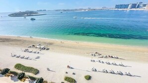 Uma praia com espreguiçadeiras e guarda-sóis, mar azul cristalino e edifícios ao longe.