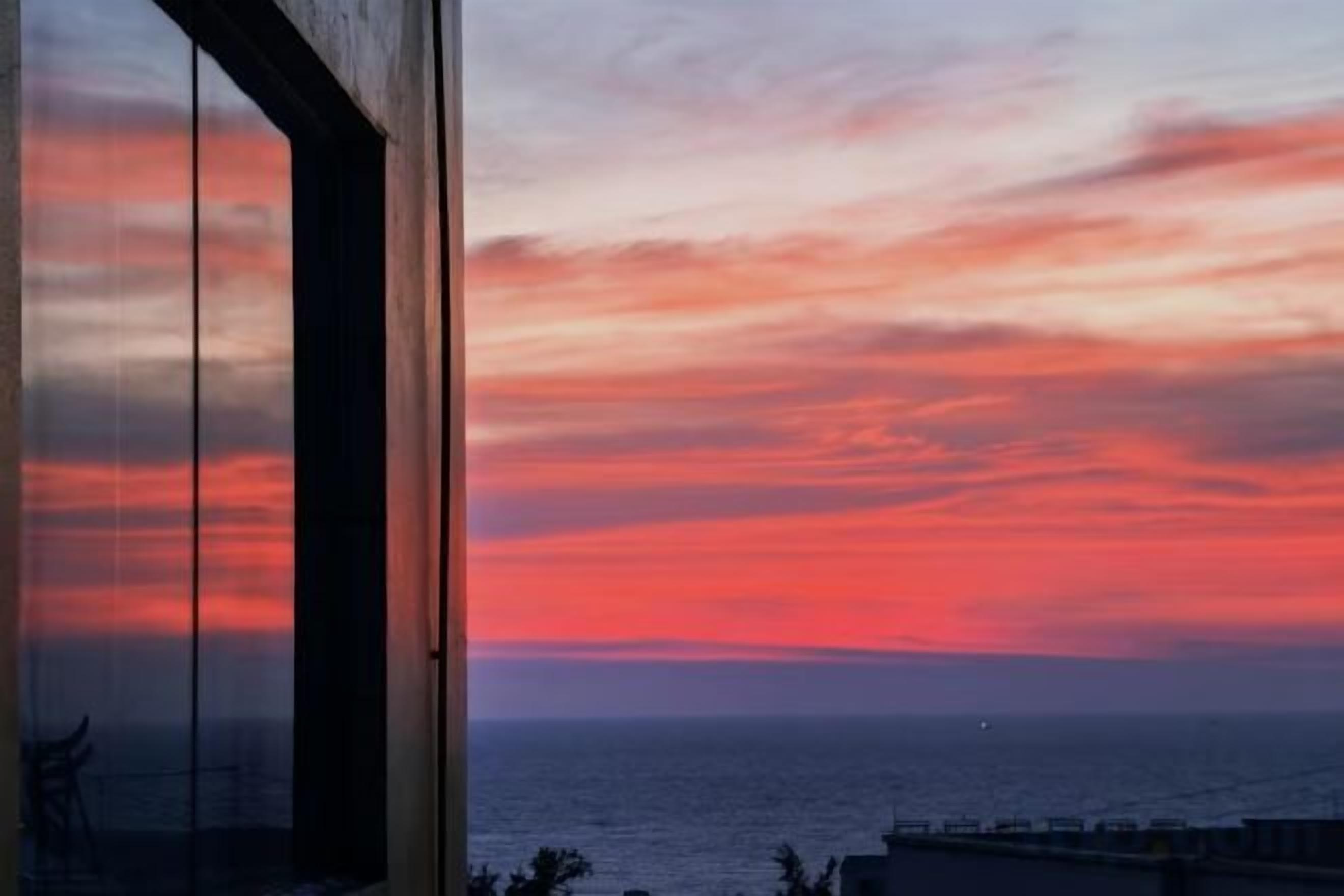 Vista al atardecer desde una ventana con vista al mar.