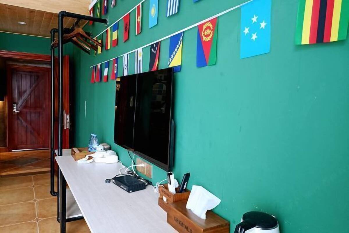 Una habitación con pared verde, un televisor de pantalla plana sobre una mesa de madera y una puerta al fondo.